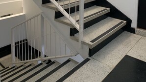 Una escalera con barandillas blancas y peldaños negros que conduce a una puerta con manija.