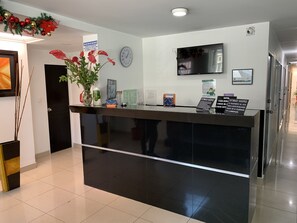 A hotel reception desk with a clock, a television, and a sign indicating check-in. - Hotel Casa Guillermo (Bogotá)