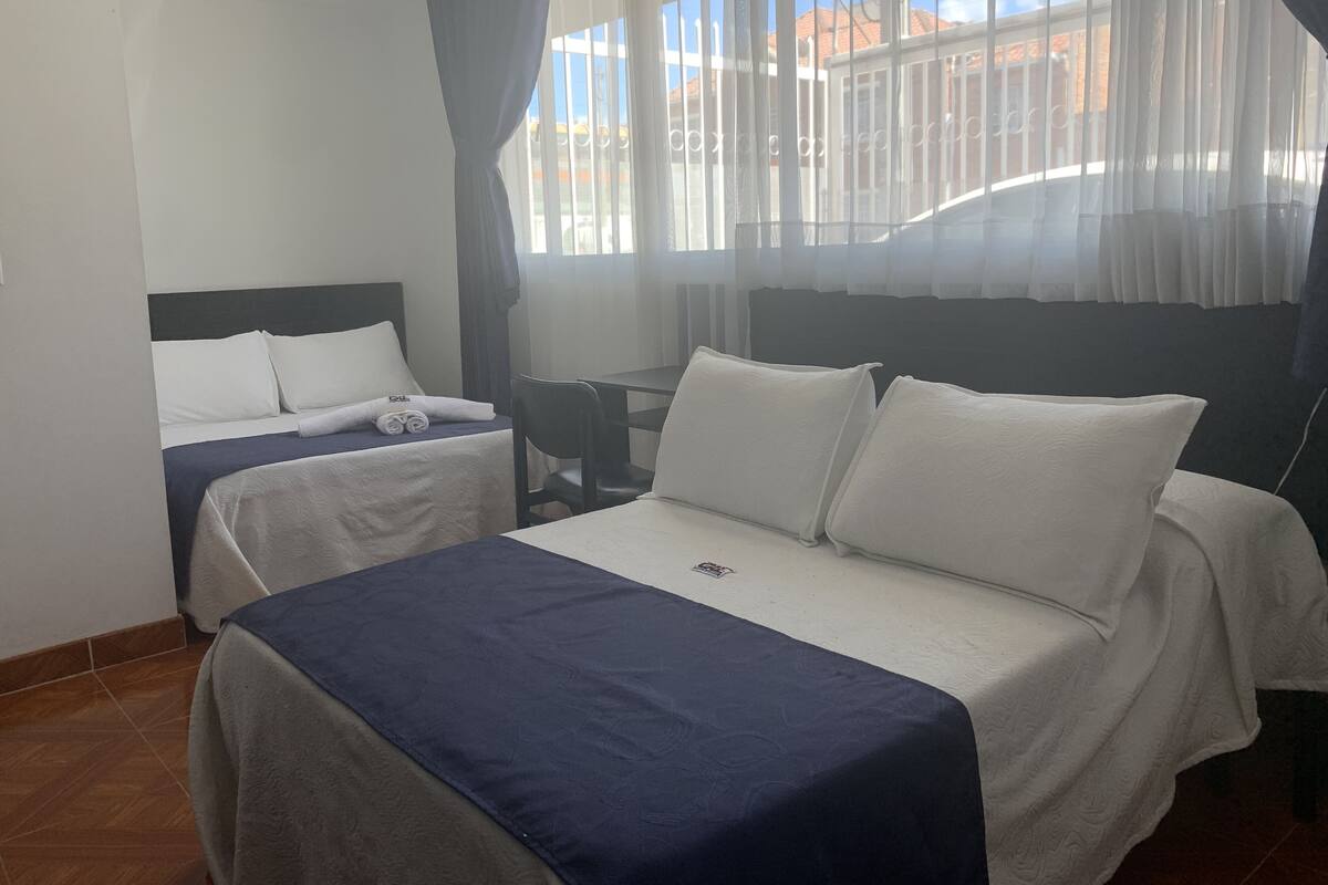 Habitación de hotel con dos camas, un escritorio y una ventana con cortinas.
