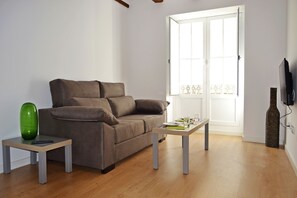 Una sala de estar con un sofá, dos mesas, un jarrón verde y un televisor.