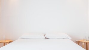 Habitación de hotel minimalista con una cama individual, dos mesitas de noche y una pared blanca lisa.