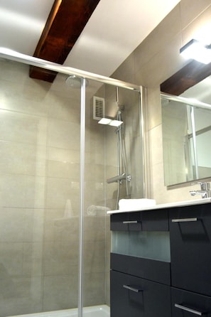 Un baño moderno con cabina de ducha de vidrio, un espejo grande y muebles oscuros.