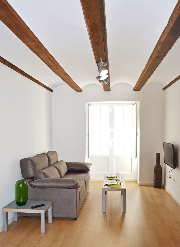 Una sala de estar con un sofá, una mesita, un jarrón verde y un televisor en la pared.