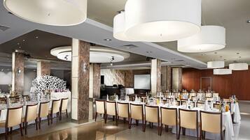 A spacious dining area with multiple tables set for a meal, large ceiling lights, and a modern interior design.
