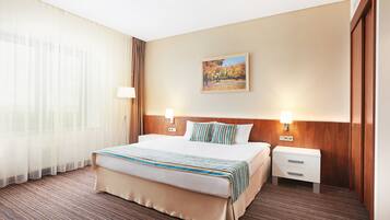A hotel room with a large bed, two bedside tables, a nightstand, a wall-mounted lamp, and a painting.
