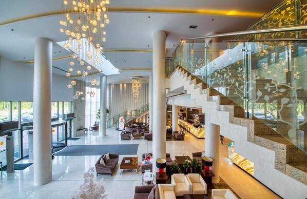 A spacious lobby with a grand staircase, seating areas, and a reception desk.