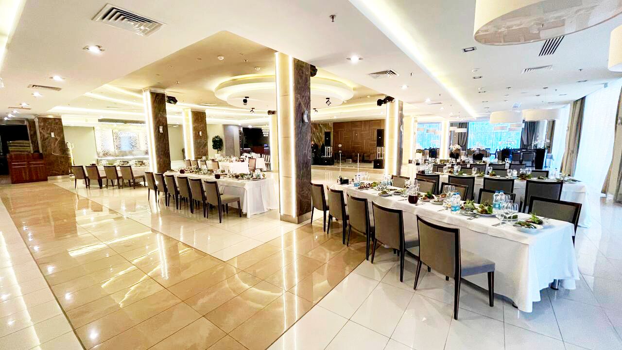 A spacious banquet hall with multiple round tables set for dining, featuring white tablecloths and chairs.