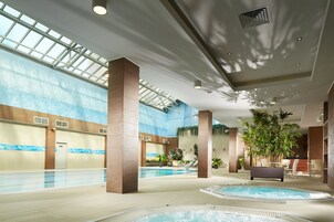 Un área de piscina interior con un tragaluz amplio, varias zonas de estar y un jacuzzi.