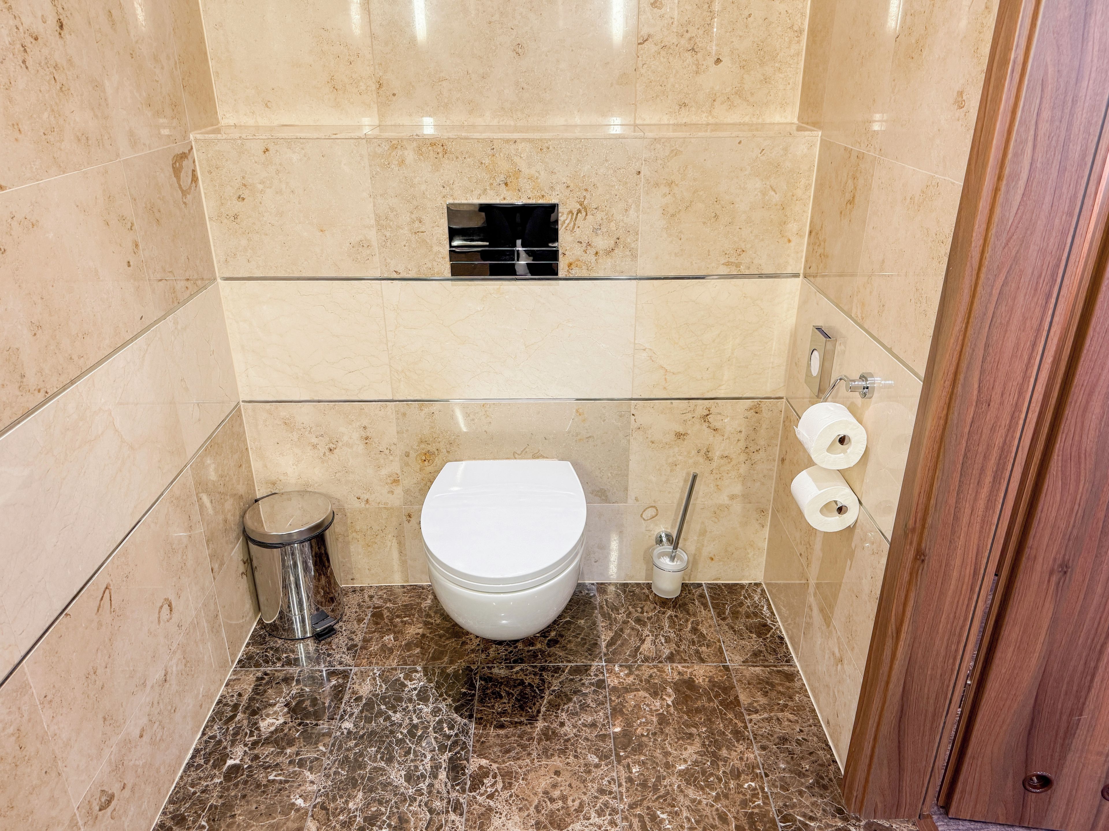 Un baño con inodoro, un cubo de basura y dos rollos de papel higiénico en la pared.