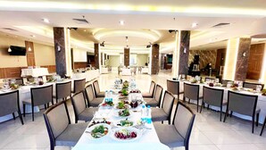 Un comedor espacioso con varias mesas dispuestas para comidas, destacando una mesa larga en el centro y mesas más pequeñas a ambos lados.