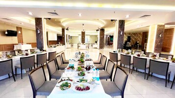 Un comedor espacioso con varias mesas dispuestas para comidas, destacando una mesa larga en el centro y mesas más pequeñas a ambos lados.