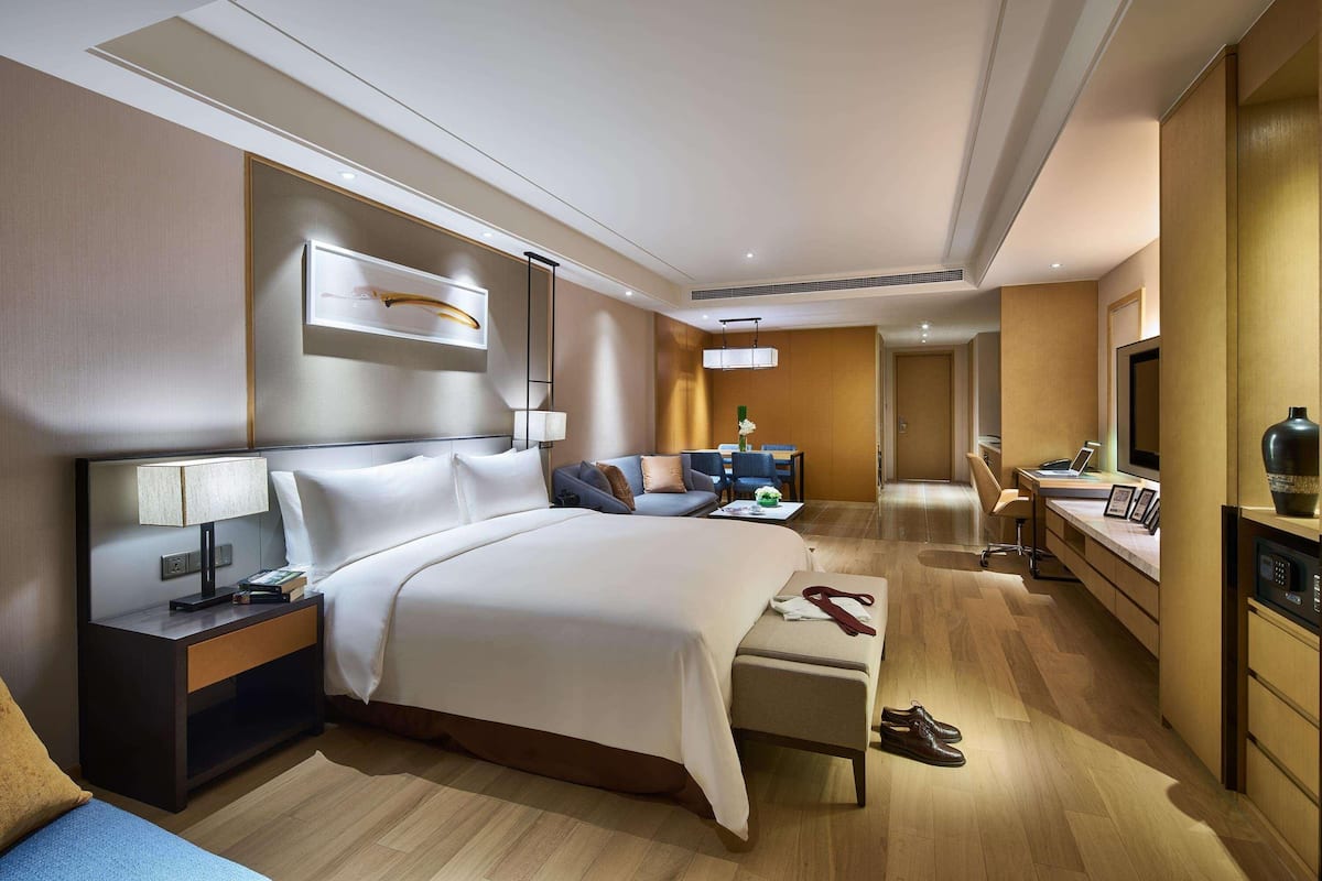 A modern hotel room with a large bed, bedside table, desk, and chair.