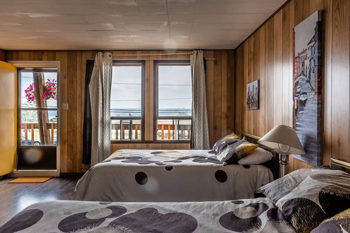 Un dormitorio con una cama, una mesita de noche, una lámpara, una ventana con cortinas y un cuadro en la pared.