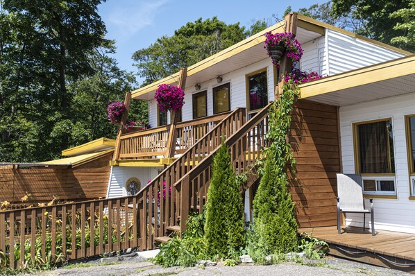 Een huis met twee verdiepingen, een houten terras, een balkon met bloembakken en een voortuin.