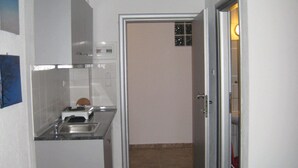 A compact kitchen with a sink, a toaster, and cabinets. There is a small trash bin and a door leading to another room. - Philoxenia Evgenia (Volvi)