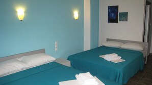 Two single beds with teal bedding, white pillows, and folded white towels. There are wall-mounted lights and two framed pictures on the wall. - Philoxenia Evgenia (Volvi)