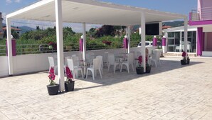 An outdoor patio with white tables and chairs, covered by a white canopy, and potted plants. - Philoxenia Evgenia (Volvi)