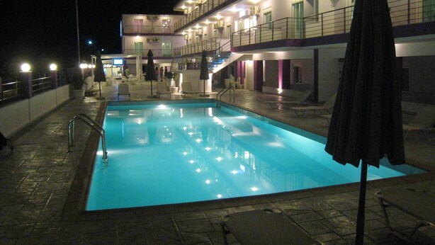A swimming pool with a tiled deck, a covered seating area, and a building with multiple balconies and windows. - Philoxenia Evgenia (Volvi)