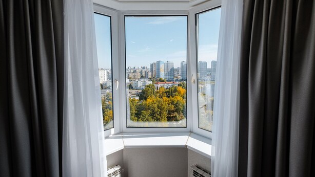 Een kamer met erker die uitkijkt over een stadsgezicht en herfstkleuren.