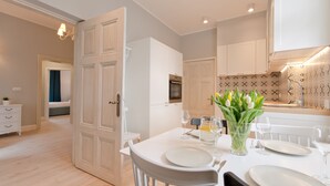 Una cocina moderna con armarios blancos, un comedor con una mesa preparada para dos personas y un jarrón de tulipanes sobre la mesa.