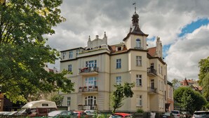 Un edificio de varios pisos con balcones, coches estacionados y cielo despejado.