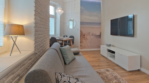 Una sala de estar moderna con un sofá, televisor y un mural en la pared con una playa.