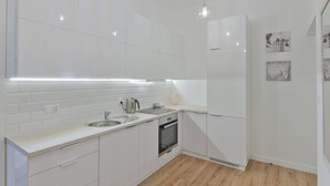Una cocina moderna con armarios blancos, un lavamanos de acero inoxidable, un horno e iluminación colgante.