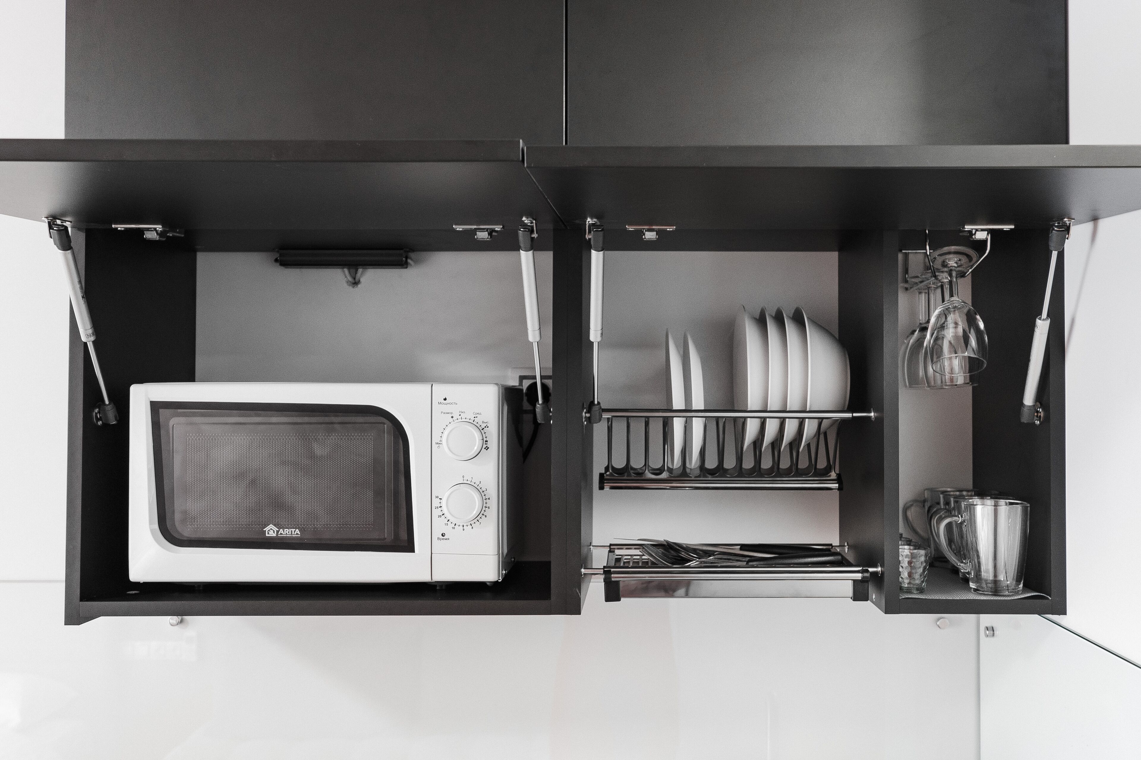A kitchen with a microwave, a dish rack, and a glass mug.