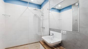 Un baño moderno con cabina de ducha de vidrio, un lavamanos blanco y un espejo sobre él.