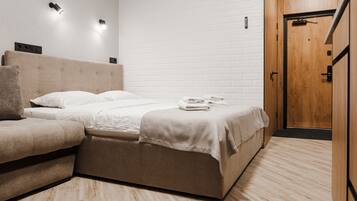 A modern hotel room with a bed, a sofa, and a wooden door.