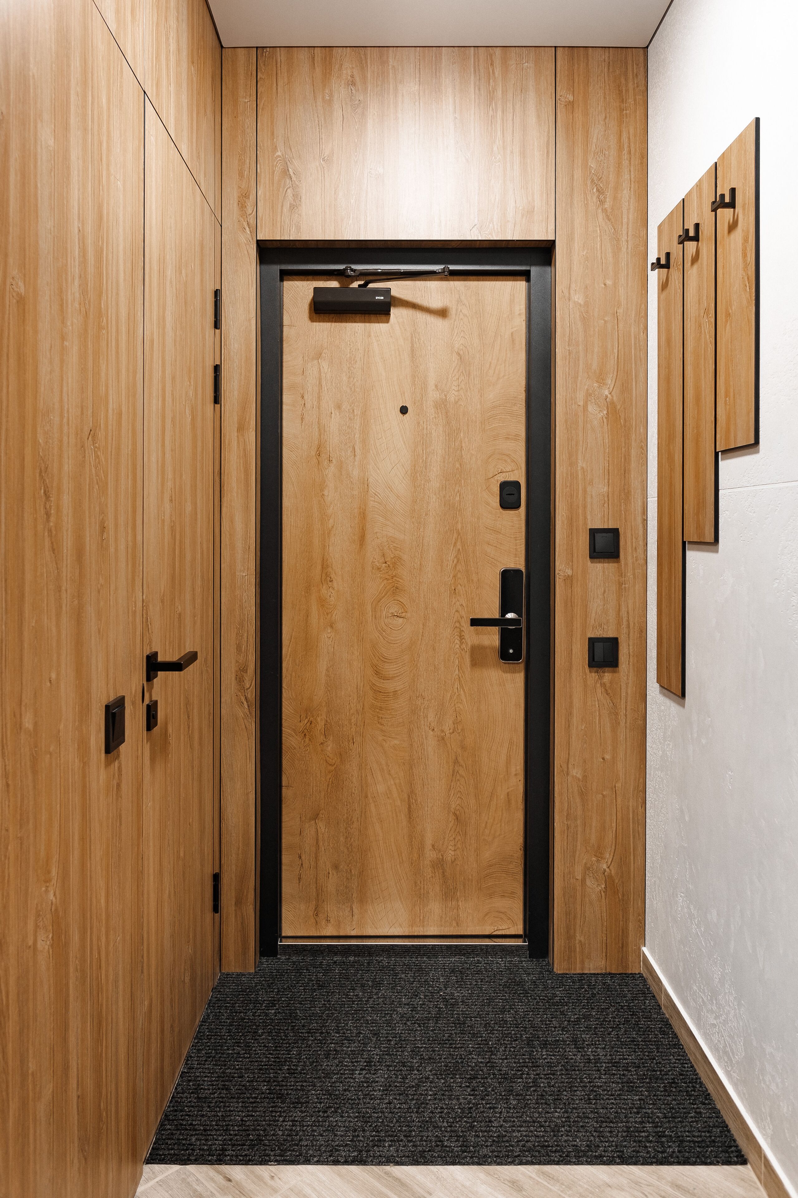A wooden door with a black frame and a handle, flanked by wooden panels and a carpeted entrance.