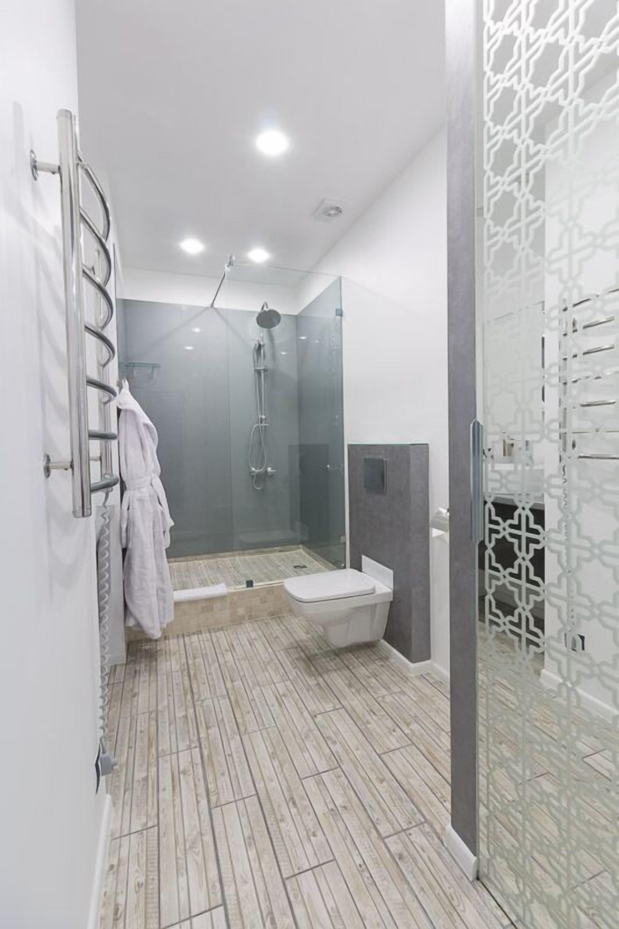 A modern bathroom with a glass shower enclosure, a white toilet, and a wooden floor.