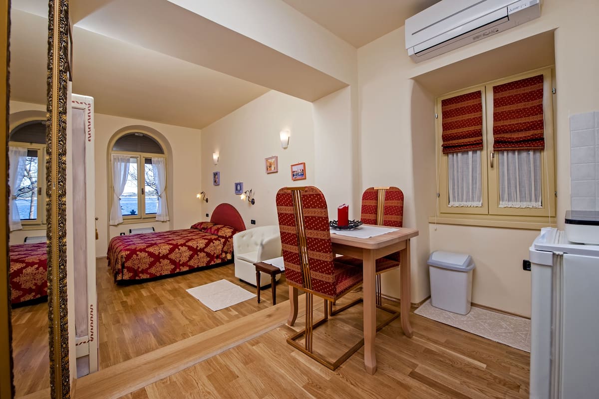 Una habitación con una cama, un escritorio y una silla. Hay una ventana con cortinas, un radiador y un cubo de basura.