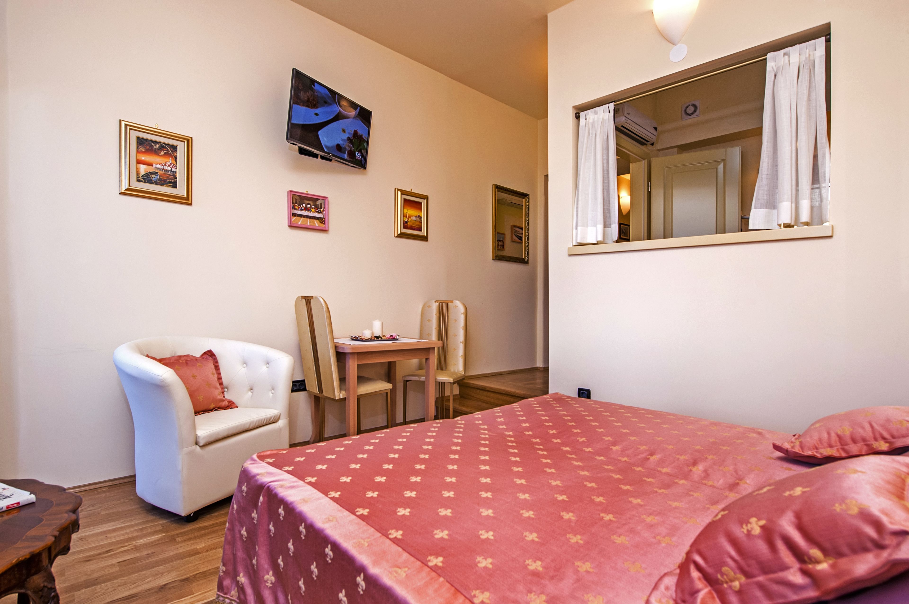 A hotel room with a bed, a chair, a table, and a TV on the wall.