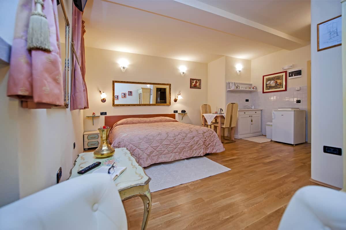 Un dormitorio con cama, mesita de noche, silla y una pequeña zona de kitchenette.