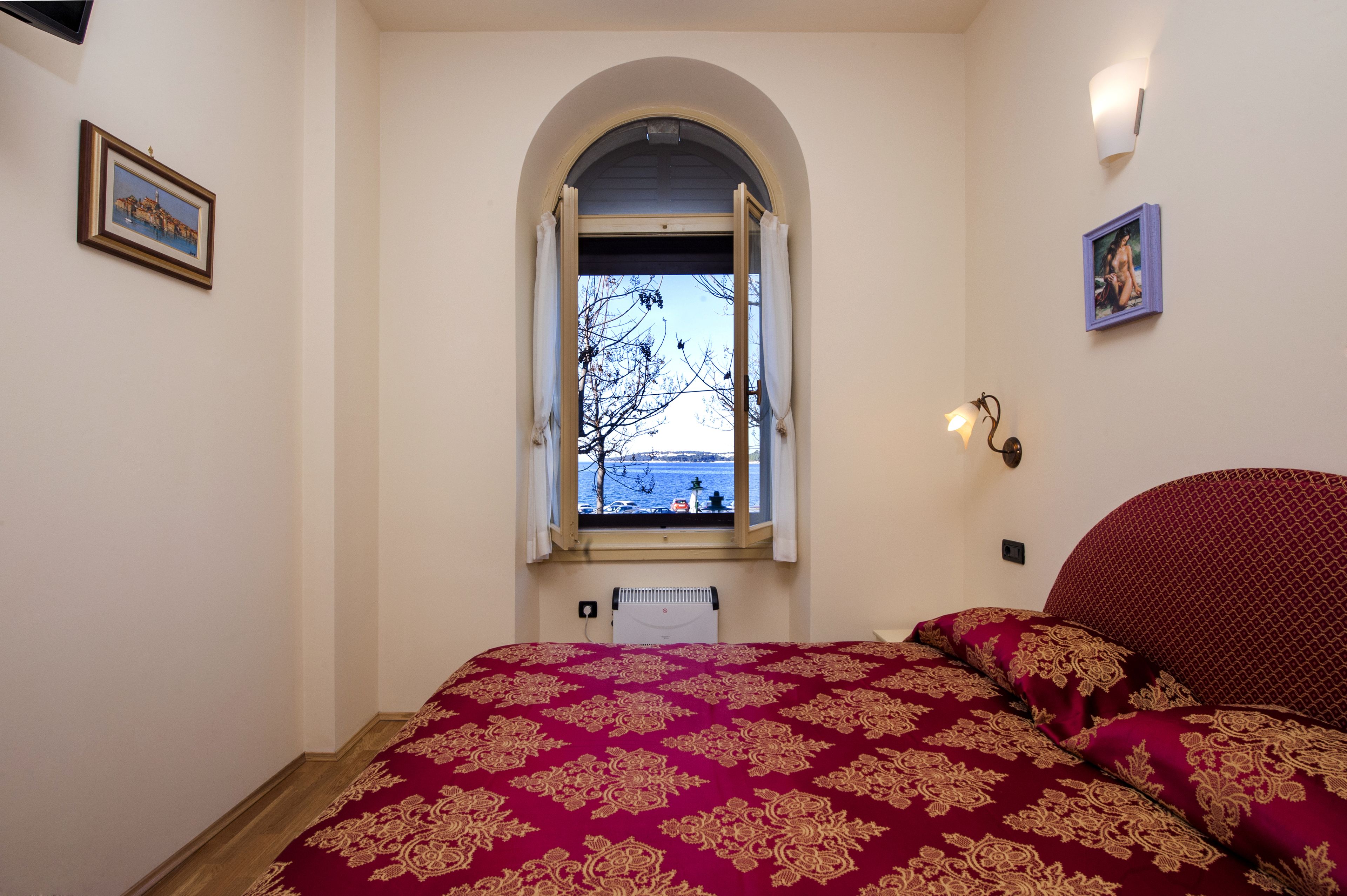 Une chambre avec un grand lit, une fenêtre avec un rideau entrouvert et une vue sur la mer.