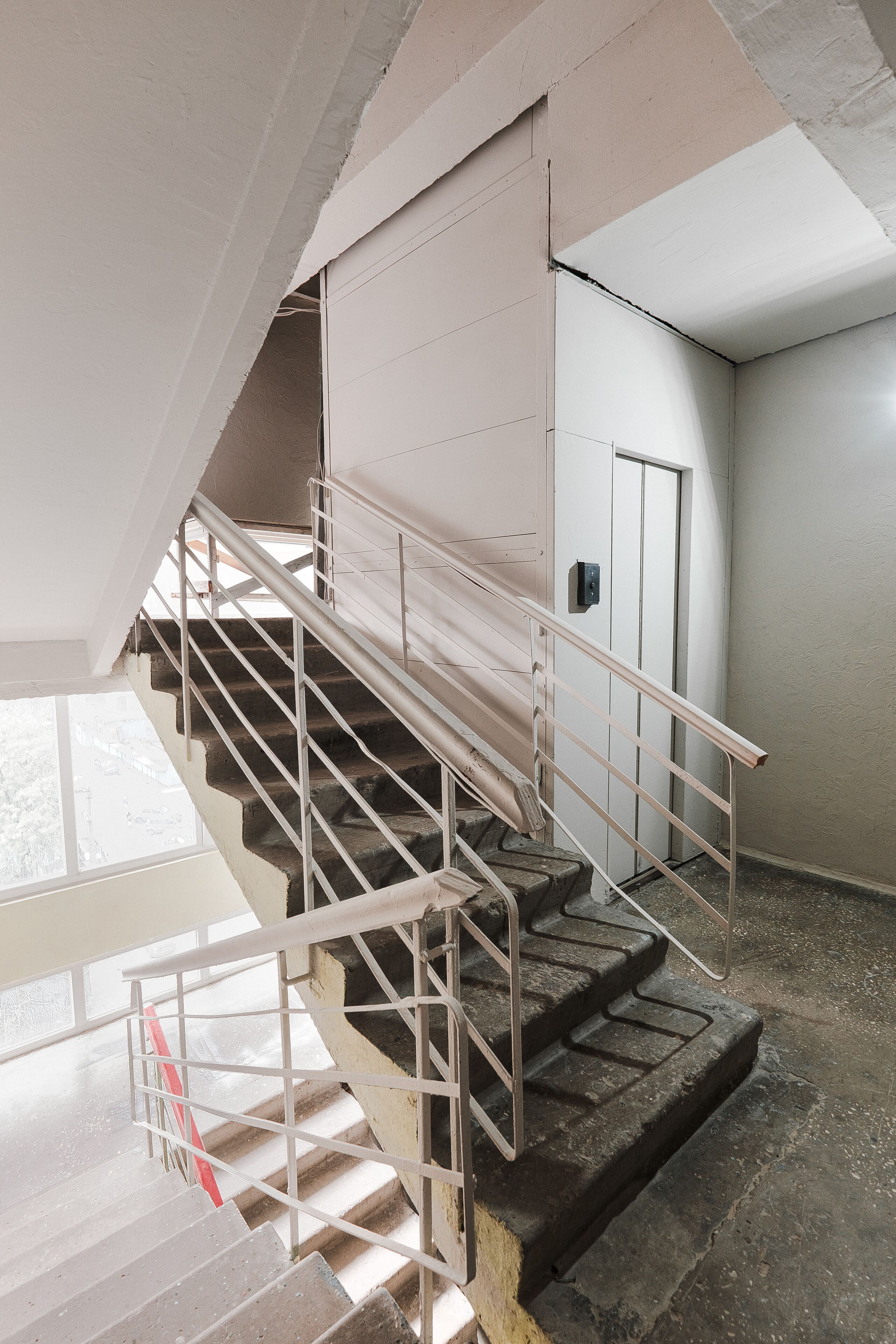 A staircase with metal railings and a handrail, leading to a door with a light switch on the wall.