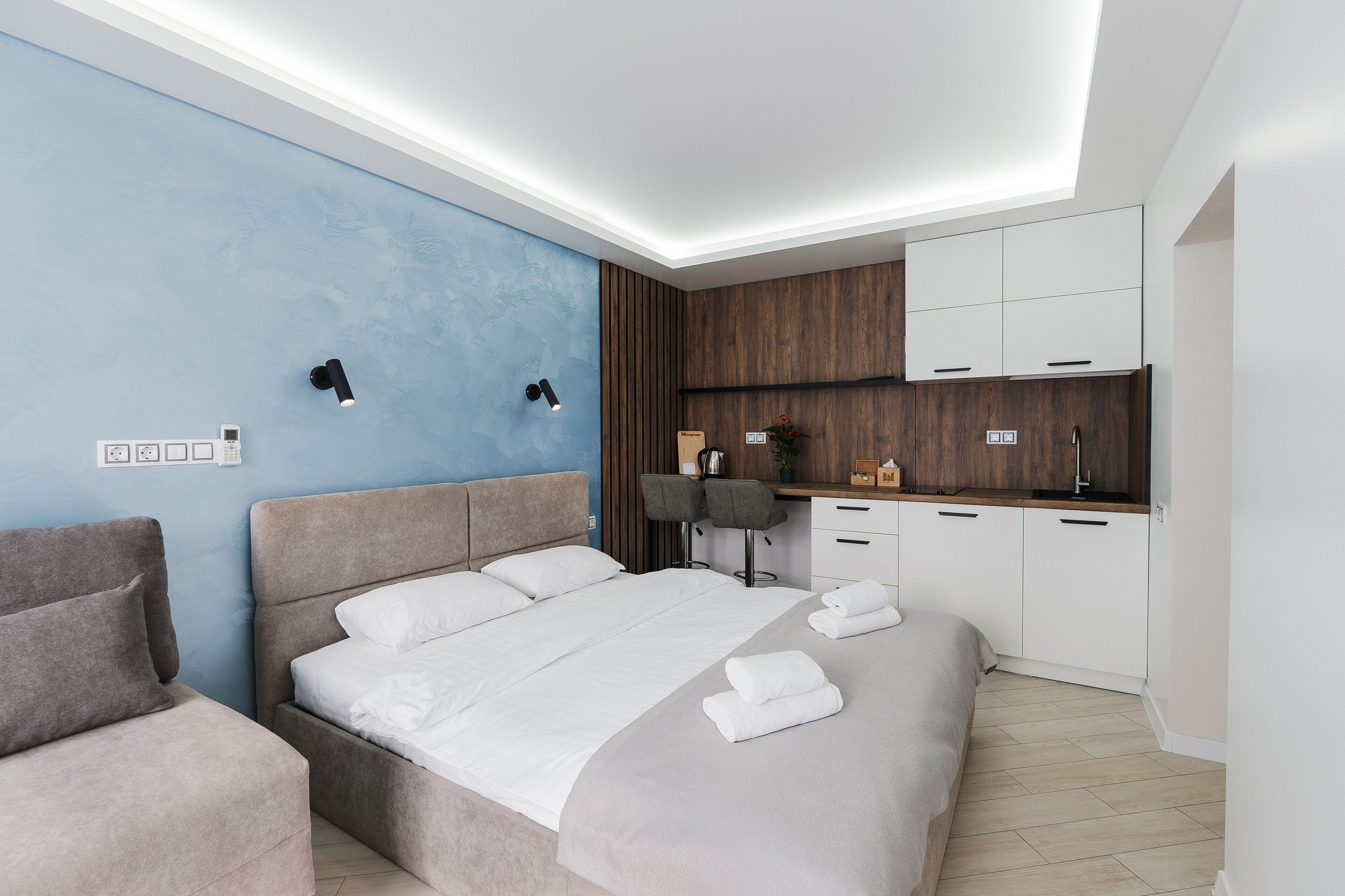 Un dormitorio moderno con una cama grande, mesitas de noche, un escritorio y una kitchenette.