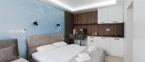 Un dormitorio moderno con una cama grande, mesitas de noche, un escritorio y una kitchenette.