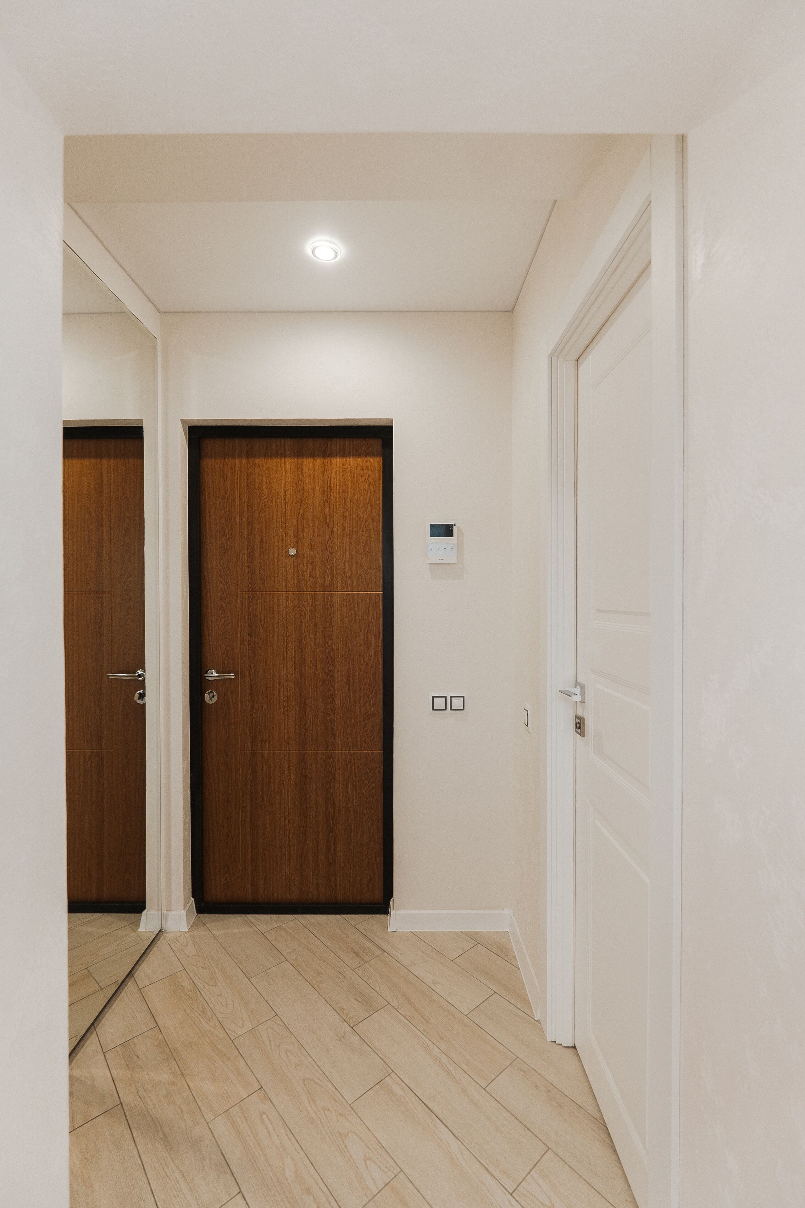 A hallway with two wooden doors, a light switch, and a thermostat on the wall.