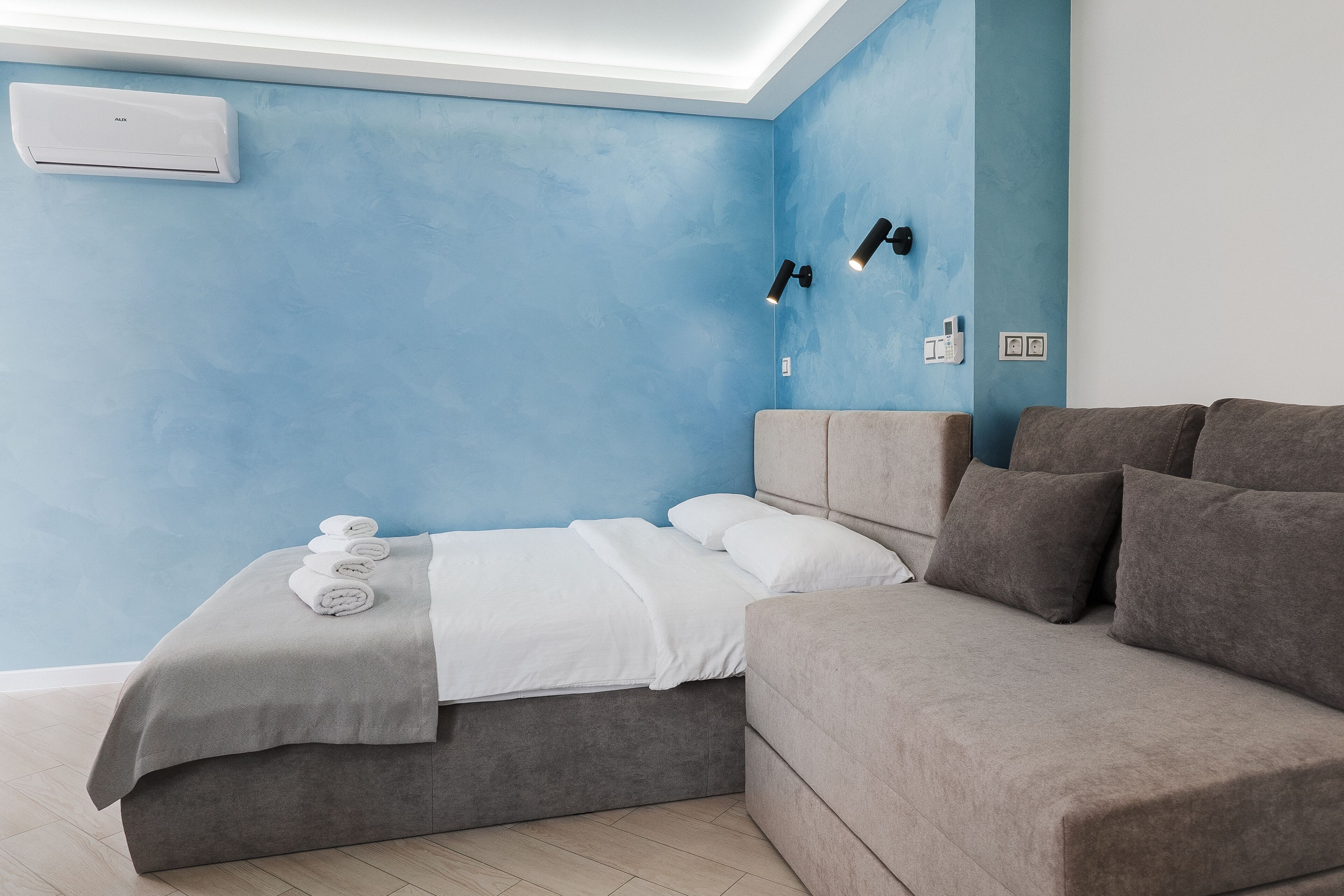 A modern bedroom with a bed, a sofa, and a wall-mounted air conditioner.