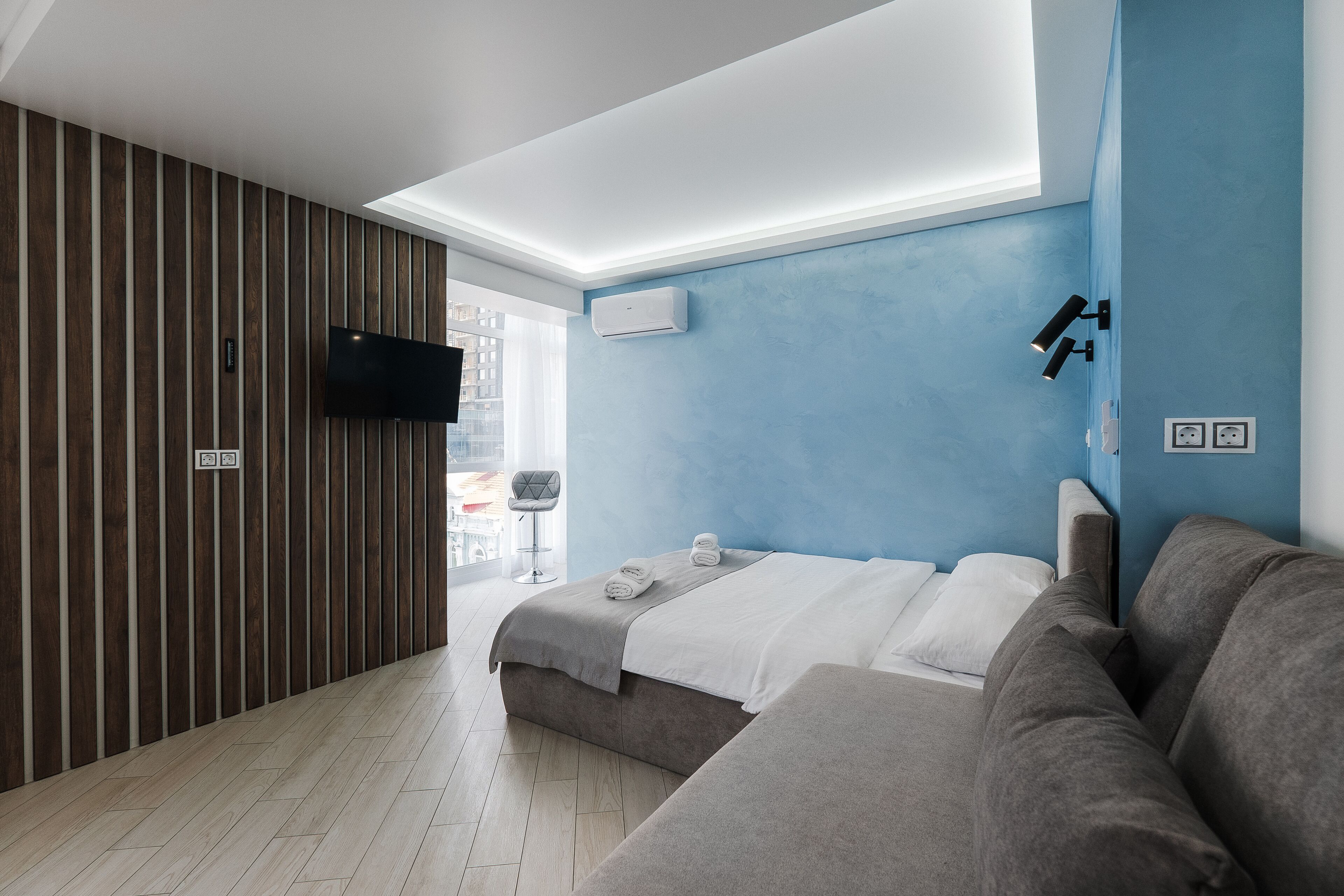 A modern hotel room with a bed, a sofa, a TV, and a window.