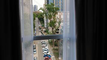A room with a large window, curtains, and a view of a parking lot and buildings.