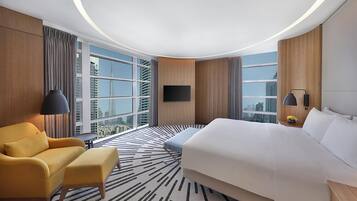 Ein Hotelzimmer mit einem großen Bett, einer Sitzecke, einem an der Wand befestigten Fernseher und Blick auf die Stadt durch große Fenster.
