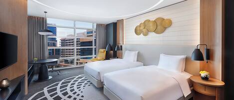 Une chambre d’hôtel avec deux lits, un bureau, une chaise, une télévision et une vue sur le paysage urbain.