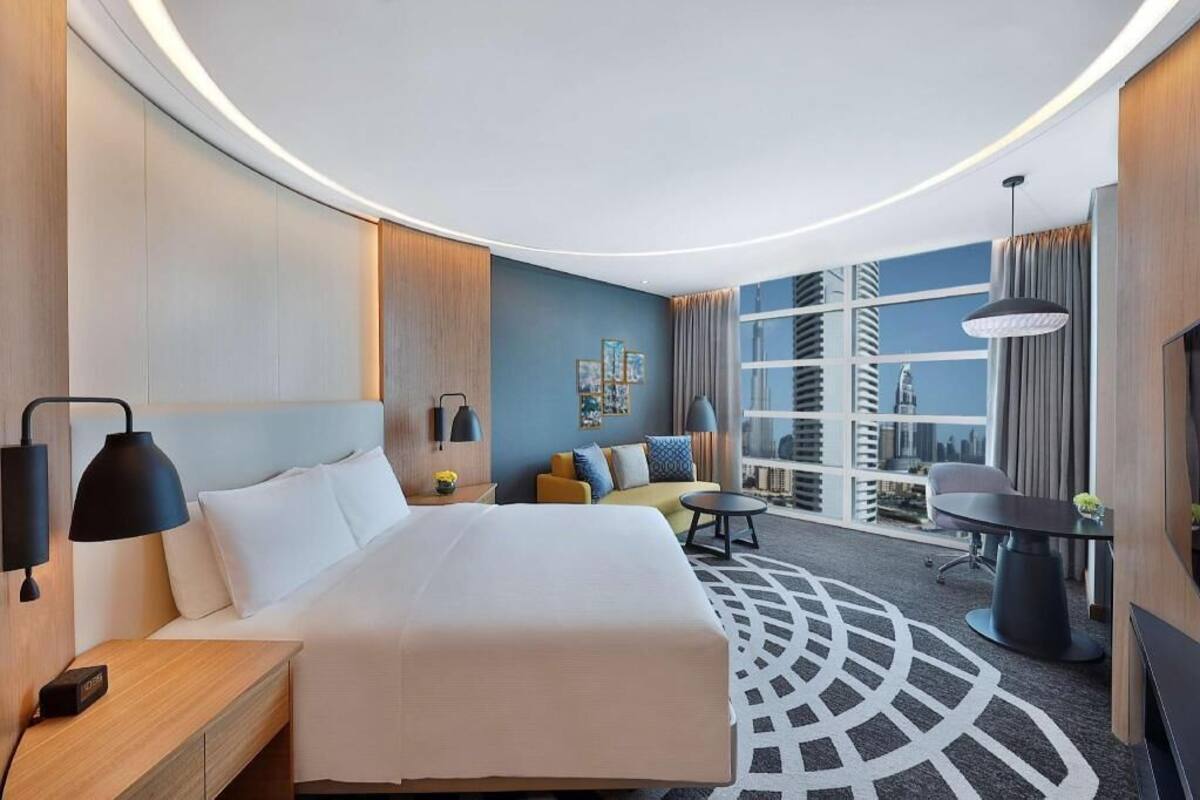 Moderni hotellihuone, jossa on suuri sänky, sohva, työpöytä ja näkymä kaupunkiin.