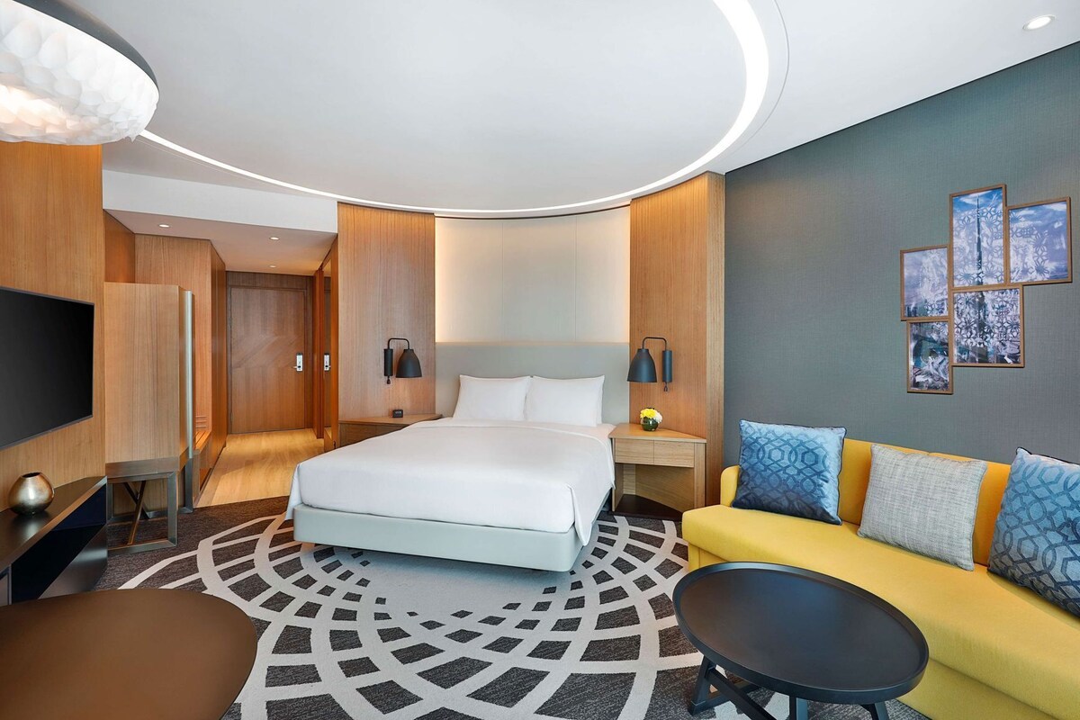 Una camera d'albergo moderna con un letto, una poltrona, una TV e una scrivania.