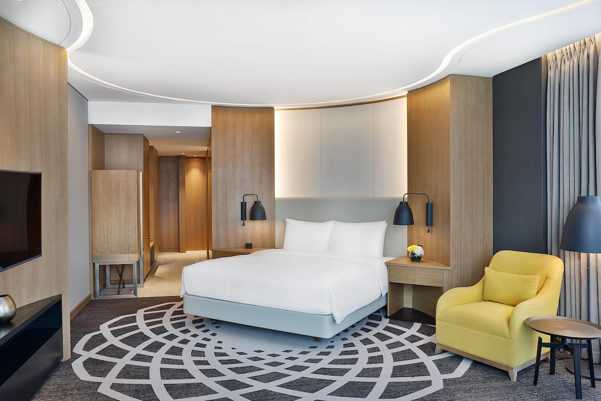 Moderni hotellihuone, jossa on suuri sänky, keltainen nojatuoli, pieni pöytä ja televisio.