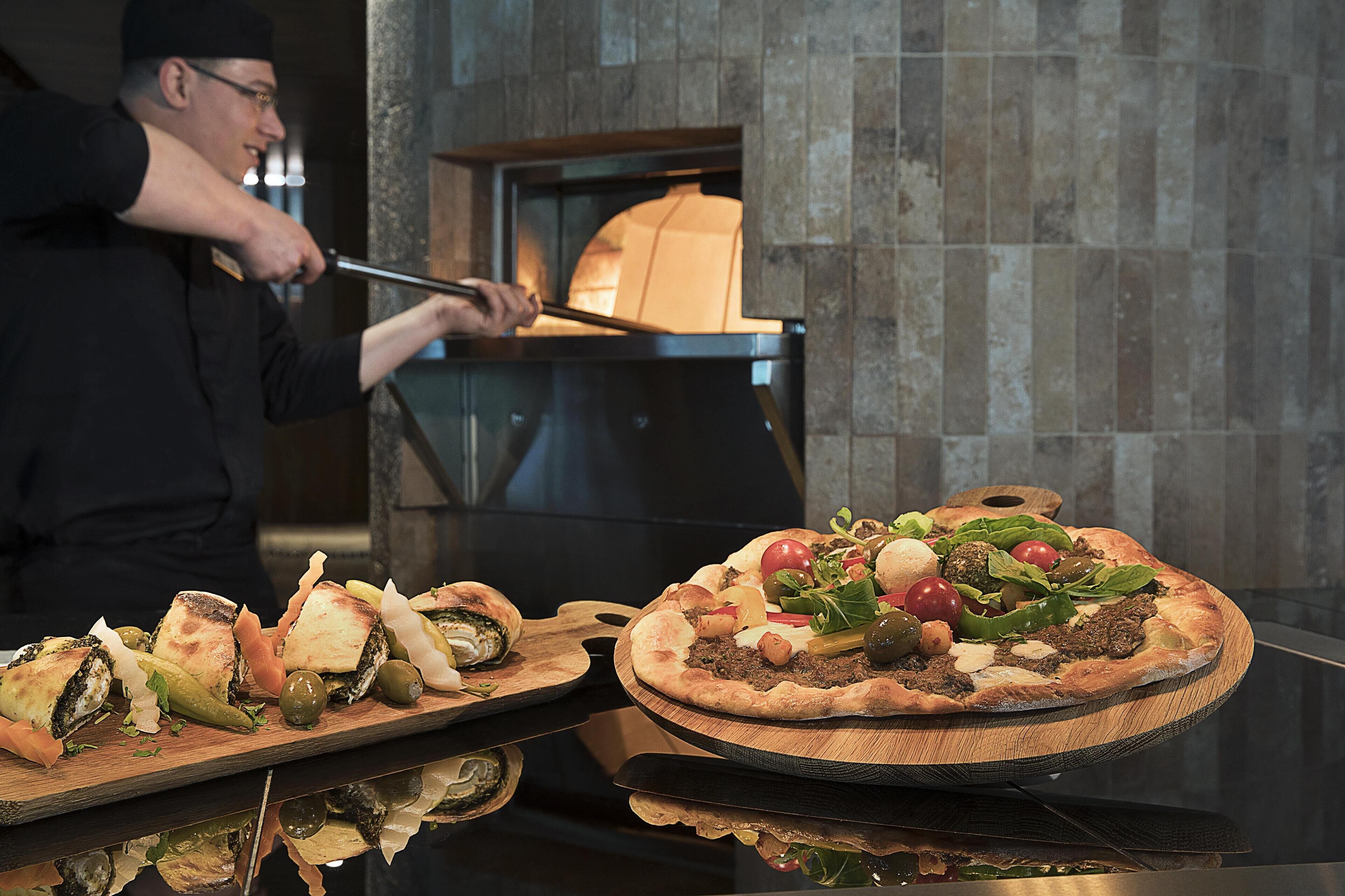 A chef preparing pizzas in a kitchen with a stone wall and a pizza oven.