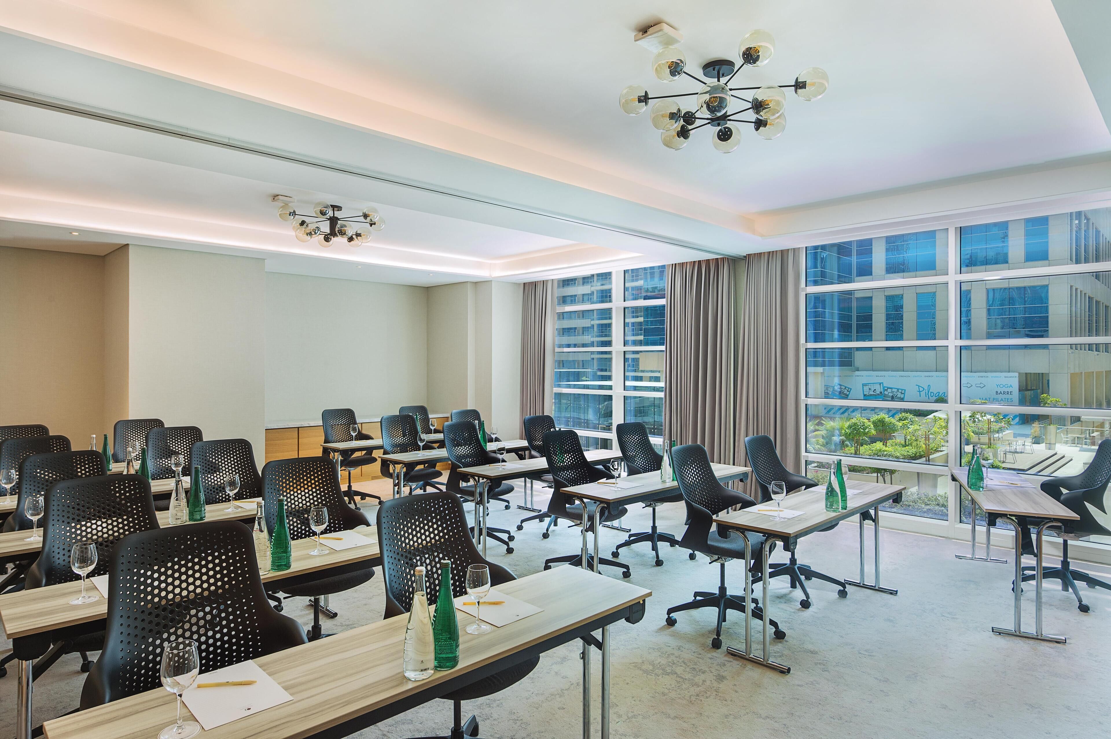Une salle de conférence dotée de plusieurs tables et de chaises, de grandes fenêtres avec des rideaux et d’un éclairage au plafond.